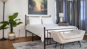 Une chambre à coucher avec un lit, une table de chevet, une lampe, une chaise et une plante en pot.