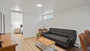 Un salon moderne avec un canapé gris, une table basse en bois et une petite table d’appoint surmontée d’une lampe.