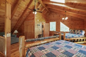 A cozy cabin bedroom with a wooden ceiling, a bed with a plaid bedspread, a wooden bench, and a ceiling fan.