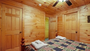 Una camera da letto con pannelli in legno, una coperta a quadri, due porte in legno e una ventola a soffitto.