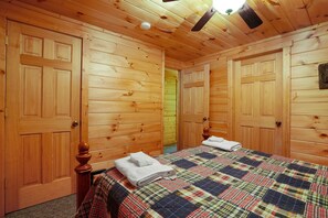 A wooden-paneled bedroom with a plaid bedspread, two wooden doors, and a ceiling fan.