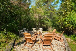 A fire pit surrounded by wooden chairs and plastic chairs in a forested area.