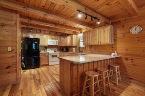 A wooden cabin interior with a kitchen featuring a black refrigerator, white stove, and wooden cabinets.