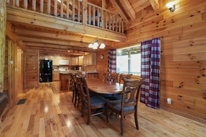 A wooden cabin interior with a dining area, kitchen, and a balcony.