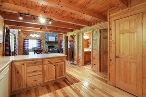 A wooden cabin interior with a kitchen area, wooden cabinets, and a large wooden door.
