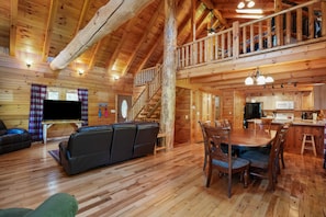 A wooden cabin interior with a living room, dining area, kitchen, and a staircase to a loft. - Pine Knoll Lodge | Hocking Hills, Hot Tub, Views (Logan)