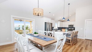A modern kitchen with white cabinets, stainless steel appliances, and a dining area with white chairs and a wooden table. - Oceanside, Private Pool, Hot Tub, WC960, Blue Heron (Corolla)