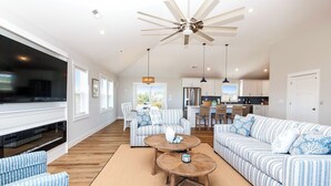 A spacious living room with a large TV, striped sofas, and a ceiling fan. - Oceanside, Private Pool, Hot Tub, WC960, Blue Heron (Corolla)