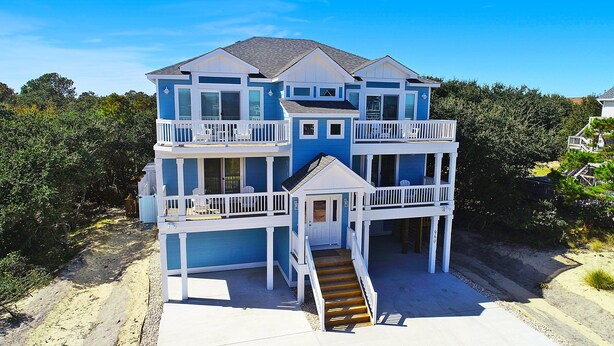 A multi-story beachfront house with a balcony on each floor, a covered front porch, and a staircase leading to the entrance. - Oceanside, Private Pool, Hot Tub, WC960, Blue Heron (Corolla)