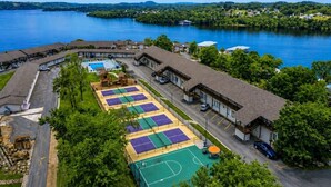 Vista aérea de una propiedad junto al lago con múltiples canchas de tenis, piscina y un edificio con zona de porche cubierta.