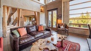 A spacious living area with a leather sofa, a rustic coffee table, and a view of a balcony. - Panoramic views | Private hot tub | BBQ | Parking (Whistler)