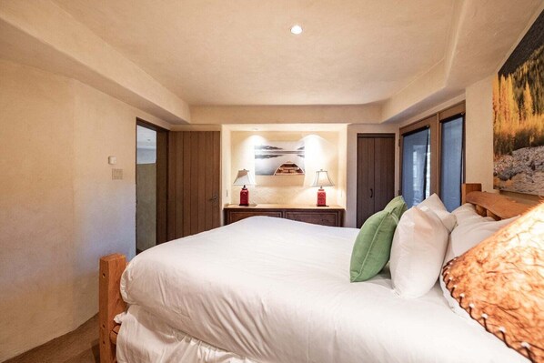 Een slaapkamer met een bed, kussens, een nachtkastje, een lamp en een schilderij aan de muur.