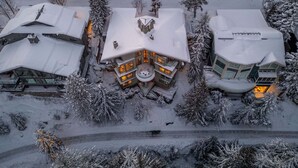 A snow-covered lodge with a central circular structure, surrounded by snow-laden trees and a clear driveway. - Panoramic views | Private hot tub | BBQ | Parking (Whistler)