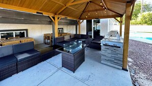 Un patio extérieur couvert, équipé d’un barbecue, d’un espace salon et offrant une vue sur une piscine.