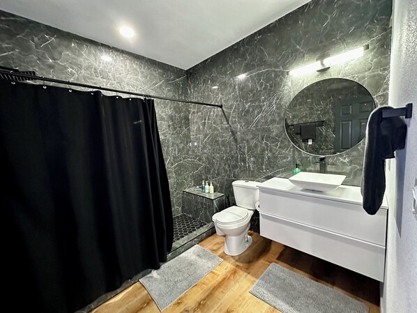 A modern bathroom with a black shower curtain, a white sink, a toilet, and a mirror.