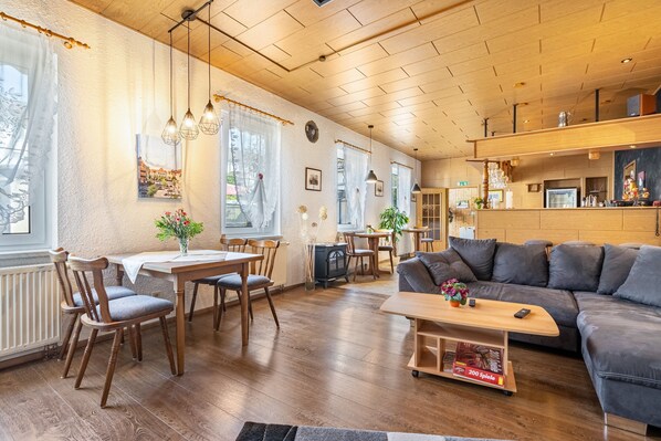 Un salon chaleureux avec un plancher en bois, un canapé, une table à manger avec des chaises et un téléviseur.
