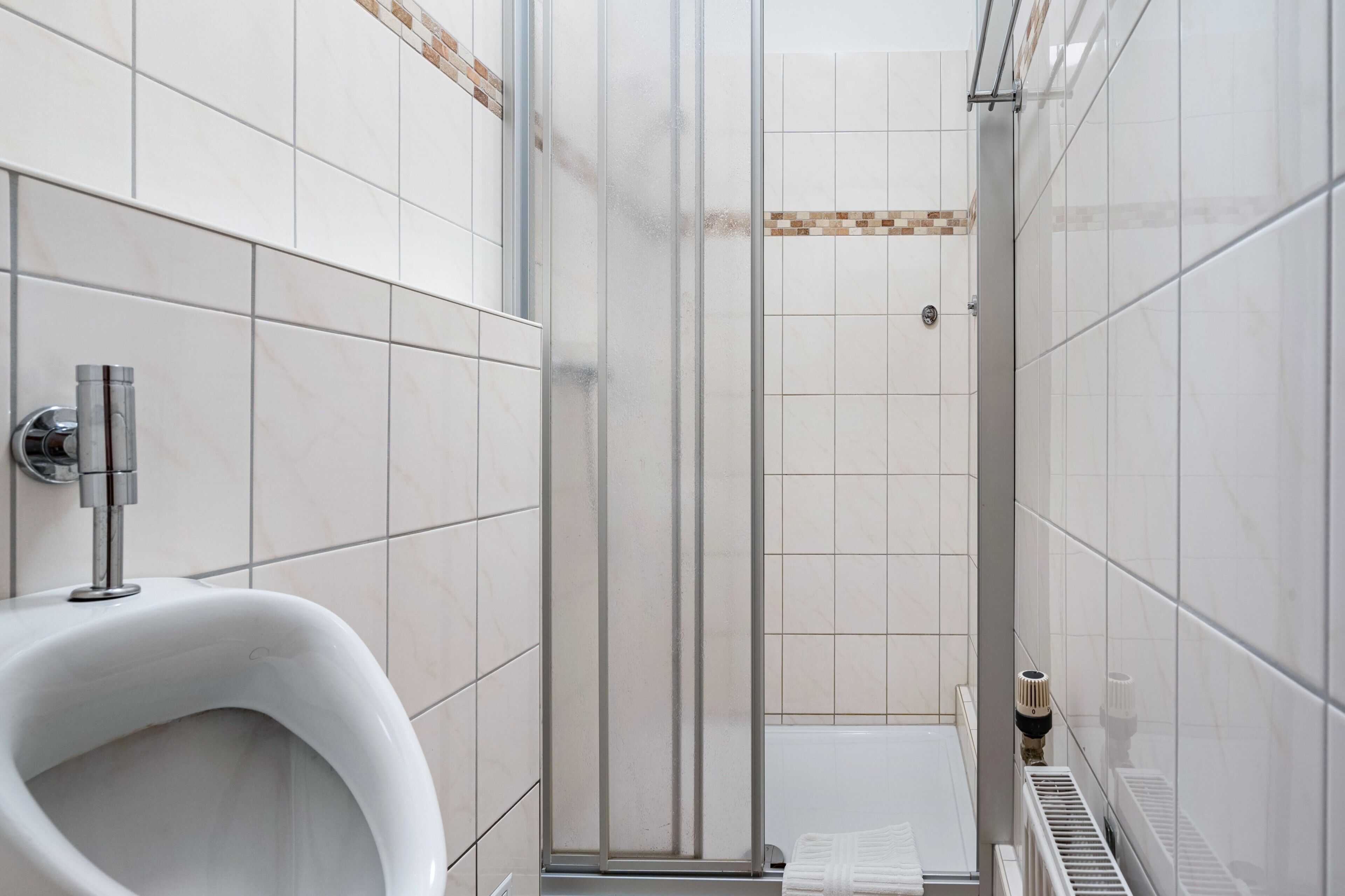 A modern bathroom with a urinal, a glass shower enclosure, and a tiled floor.