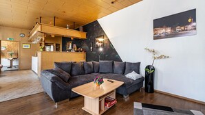 A modern hotel lobby with a wooden ceiling, a large gray sectional sofa, a wooden coffee table, a black vase with flowers, and a cityscape painting on the wall. - Holiday Apartment 'Ferienhaus Nestwärme' with Private Terrace, Private Garden and Wi-Fi (Calau)