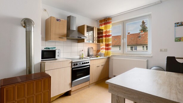 A kitchen with a microwave, oven, wooden cabinets, a window with a view, and a radiator. - Apartment 'Yellow  B' (Miltenberg)