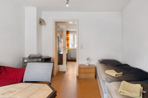 Una habitación con una cama, un escritorio, una silla, una mesita y una colcha roja.