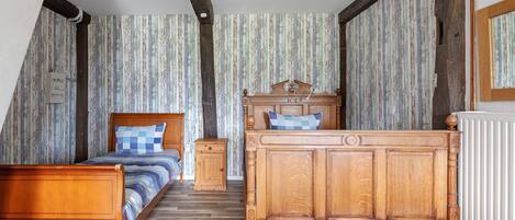 Un dormitorio con cama de madera, mesita de noche, cómoda, papel tapiz a rayas y techo inclinado.