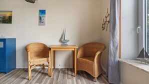 Una habitación con dos sillones de mimbre, una mesita, una ventana con cortina y un armario azul.