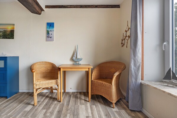 A room with two wicker chairs, a small table, a window with a curtain, and a blue cabinet.