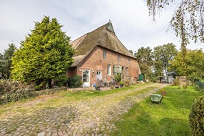 A brick building with a sloped roof, a cobblestone pathway, and a garden area with potted plants. - Room 'Das Möwennest' with Shared Terrace and Shared Garden (Barlt)