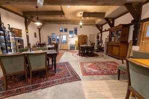 Une pièce spacieuse avec un plafond haut, des poutres en bois, un coin repas avec une table et des chaises, et un grand tapis.