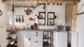 Cocina compacta con armarios blancos, microondas integrado y un refrigerador pequeño.