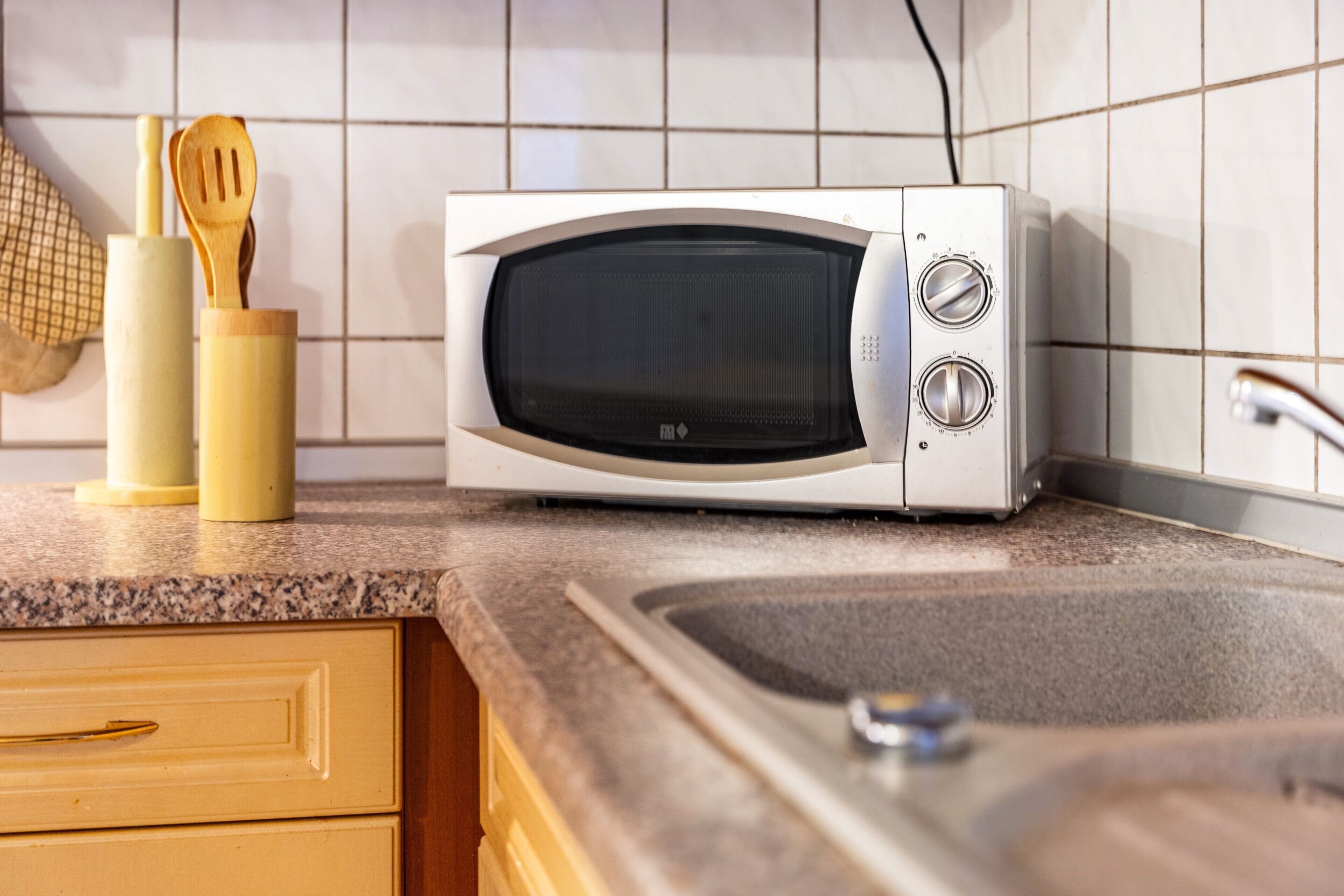 Una cocina con microondas, utensilios de madera y un lavabo.