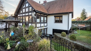 A traditional half-timbered house with a sloped roof, a garden with various plants, and a stone wall.