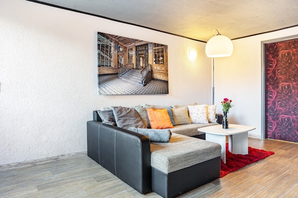 A modern living room with a sectional sofa, a white coffee table, a red rug, a floor lamp, and a large framed picture on the wall.