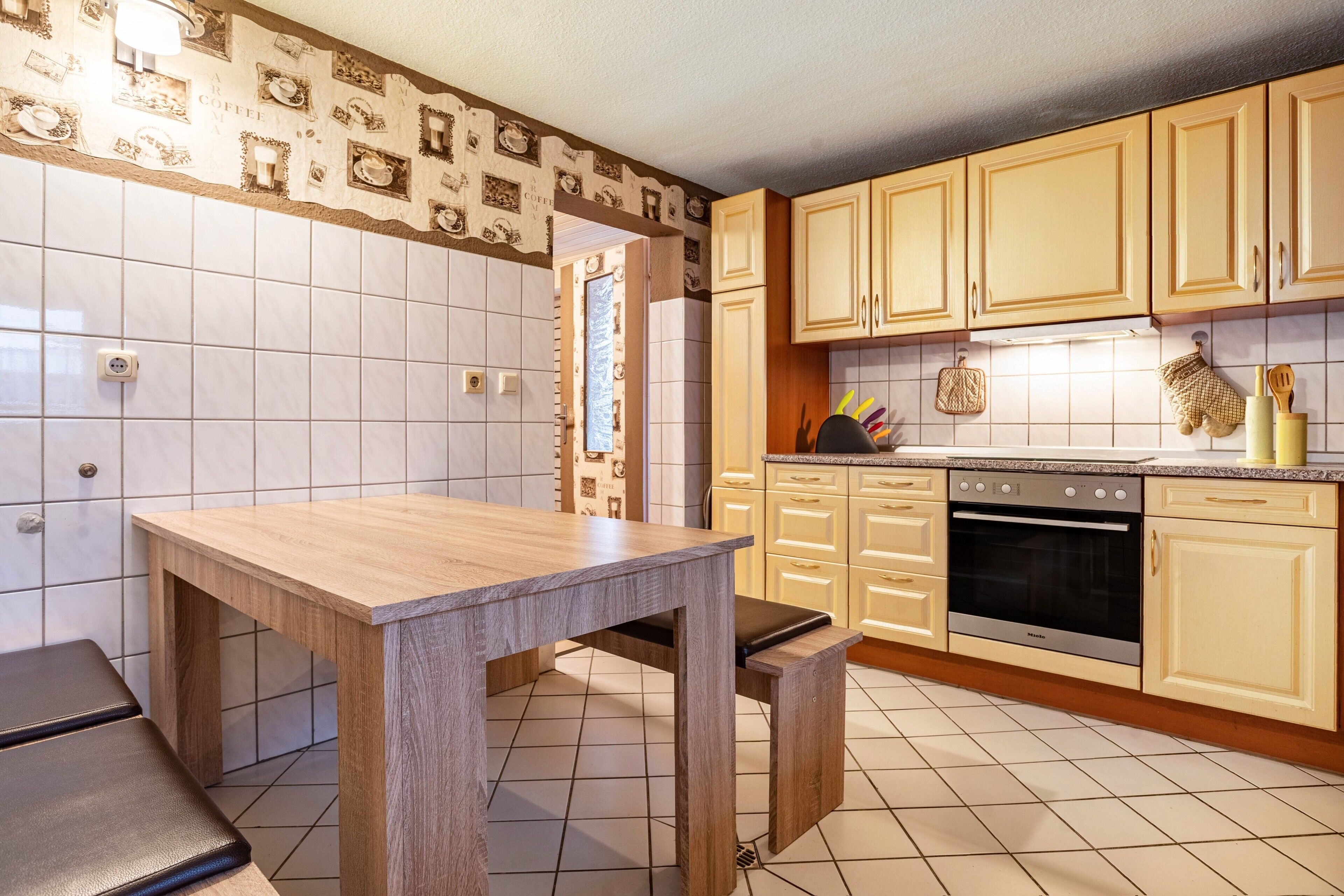 Une cuisine avec une table en bois, des placards et un sol carrelé.