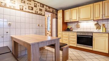 Une cuisine avec une table en bois, des placards et un sol carrelé.
