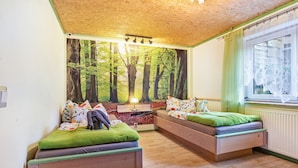 A room with two beds, a mural of a forest, a window with a curtain, and a radiator.