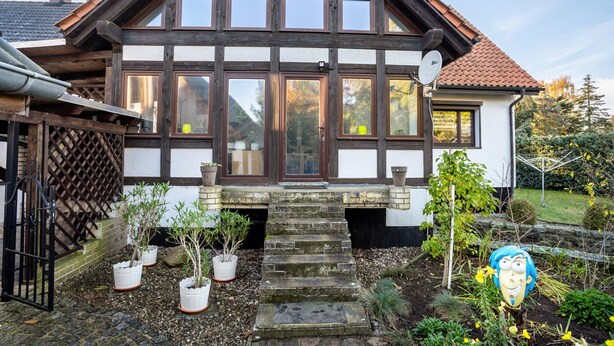 A traditional house with a steeply pitched roof, multiple windows, and a stone staircase leading to the entrance.