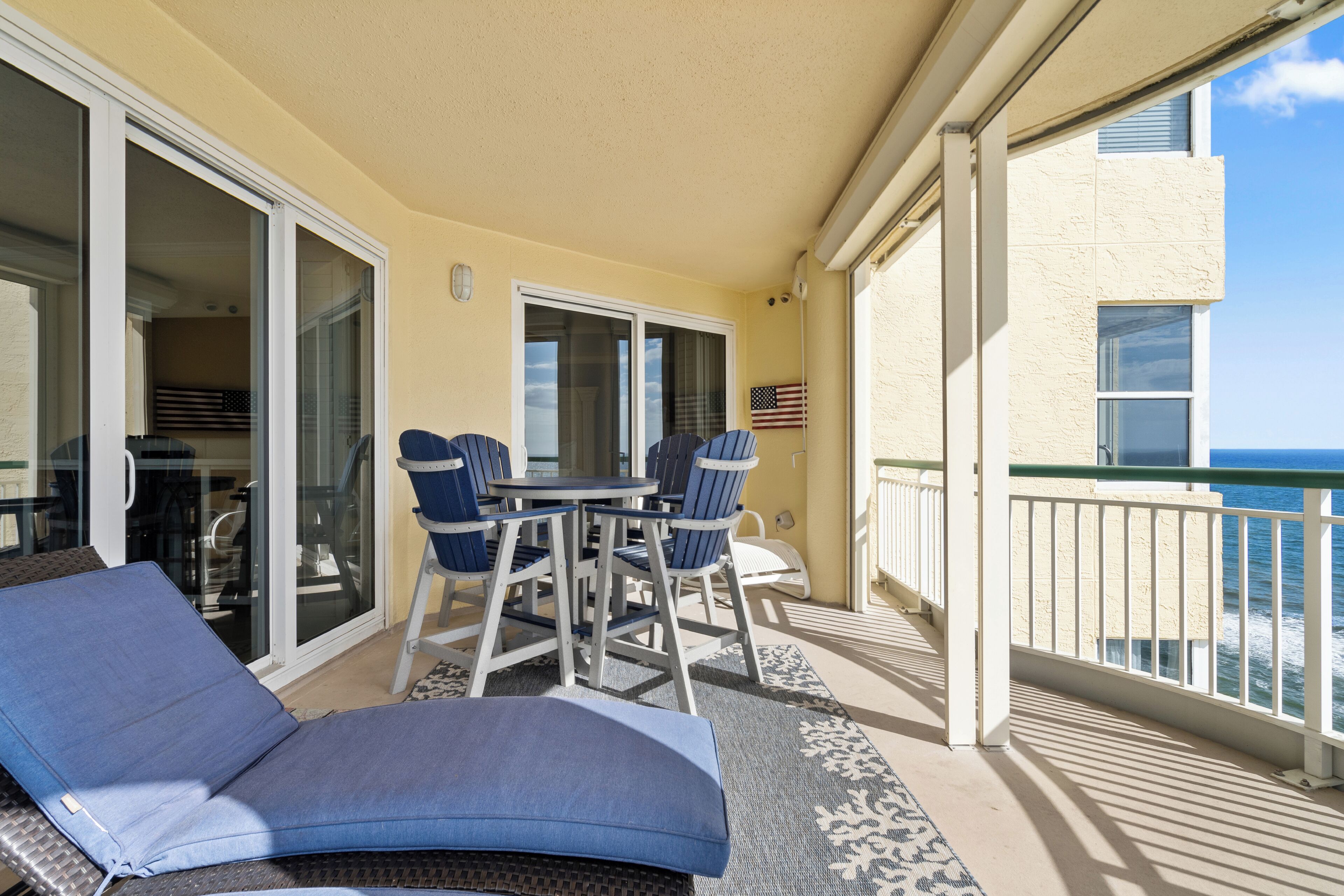 A balcony with a table and chairs, a blue cushioned chair, and an American flag.