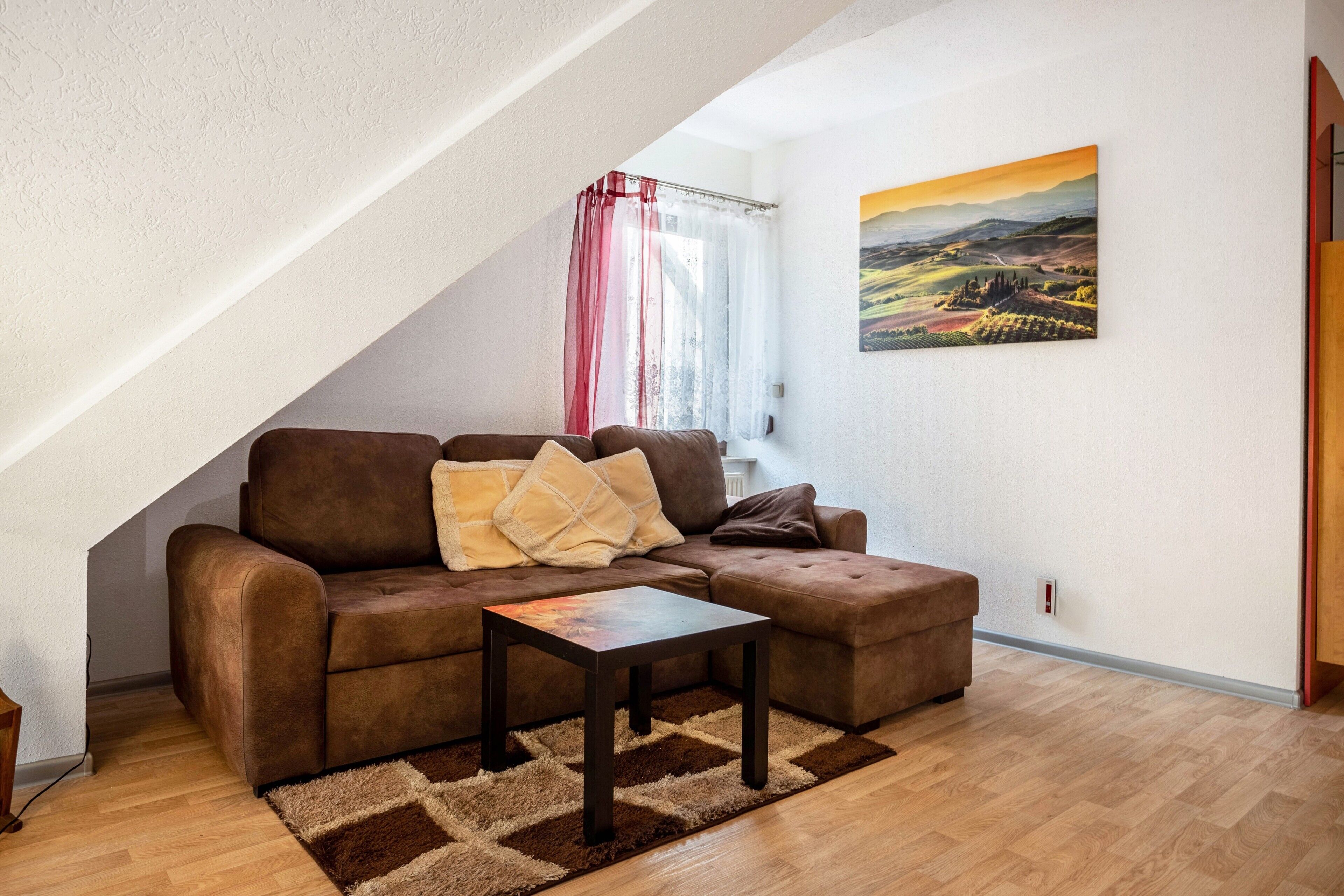 Una sala de estar acogedora con un sofá marrón, una mesita y un cuadro en la pared.