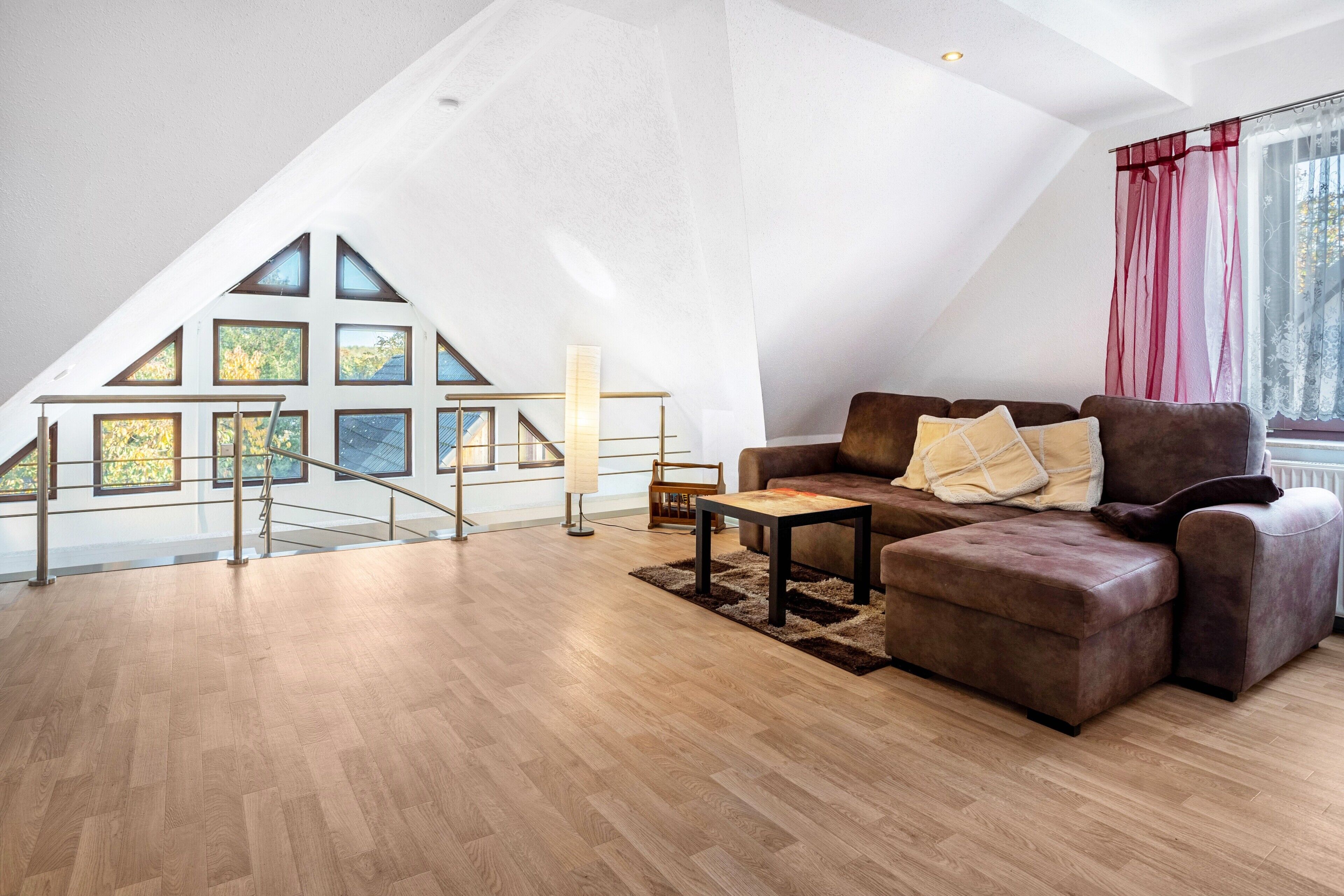 Un loft spacieux doté d’un plancher en bois, d’un canapé en cuir marron et d’un escalier menant à un balcon avec de grandes fenêtres.
