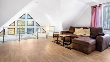 Un loft spacieux doté d’un plancher en bois, d’un canapé en cuir marron et d’un escalier menant à un balcon avec de grandes fenêtres.