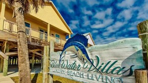 A wooden sign for Blue Water Villas with a palm tree and a building in the background.