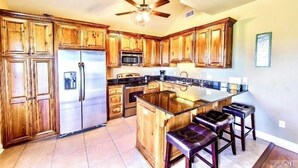 A kitchen with wooden cabinets, stainless steel appliances, a central island with bar stools, and a ceiling fan.