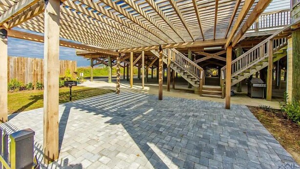 A covered outdoor area with a wooden pergola structure, a brick pathway, and a staircase leading to an upper level.
