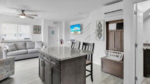 A modern kitchen with a granite island, a dining area with chairs, a sofa, and a TV mounted on the wall. - Ocean Isles Seaside Oasis (Marathon)