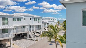 Uma fileira de casas de praia brancas com varandas, uma palmeira e um céu azul límpido.