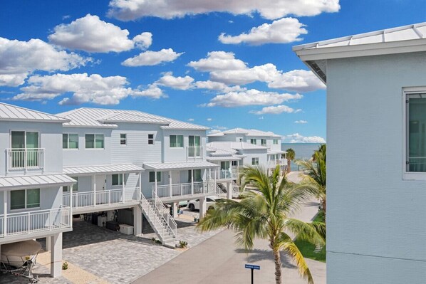 A row of white beach houses with balconies, a palm tree, and a clear blue sky.