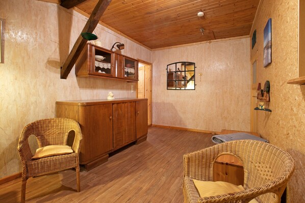 A room with wooden flooring, a cabinet, two wicker chairs, and a small window.