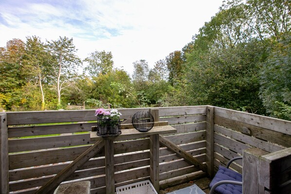 A wooden deck with a bench, a small table with a flower vase, and a birdcage.