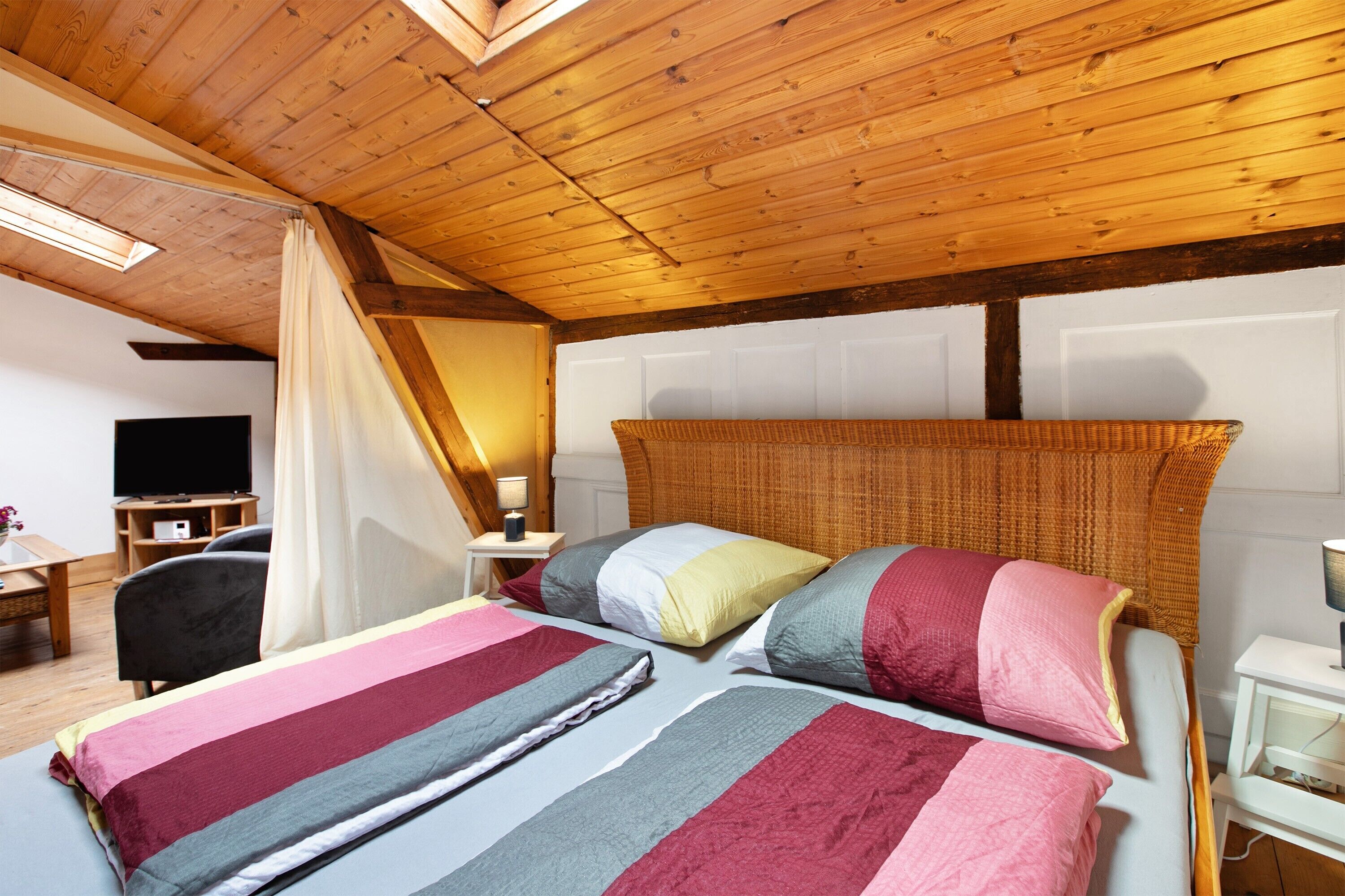 Ein Schlafzimmer mit Holzboden, einem Bett mit gestreifter Bettwäsche, einem Nachttisch und einem Fernseher.